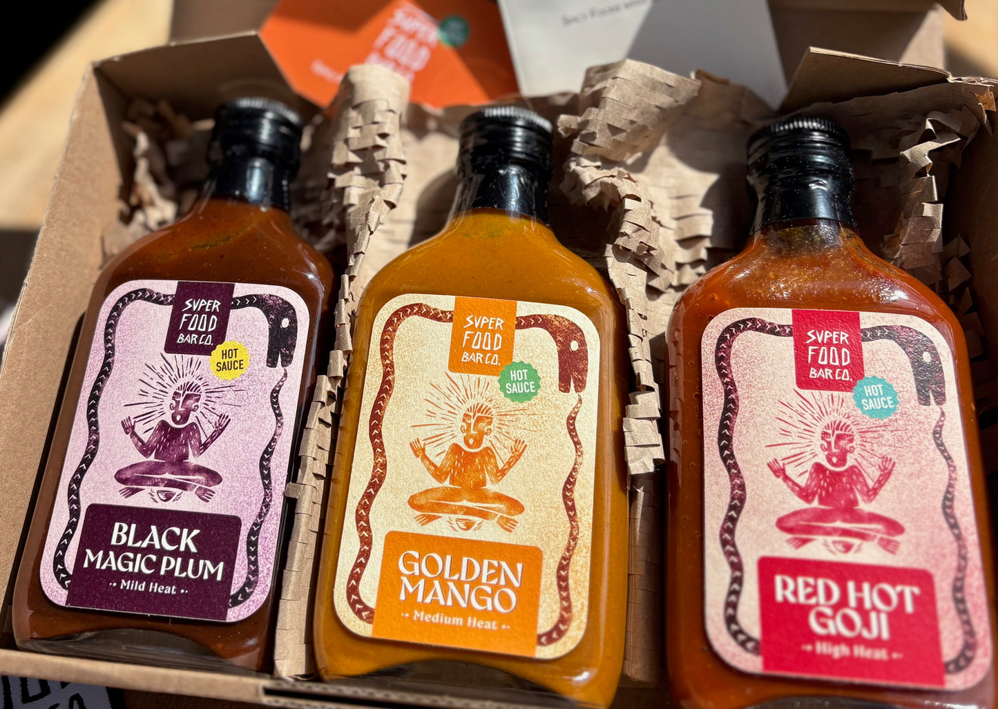 Opened gift box with three fermented hot sauces — Red Hot Goji, Golden Mango, and Black Magic Plum — in glass bottles from Superfood Bar Co.