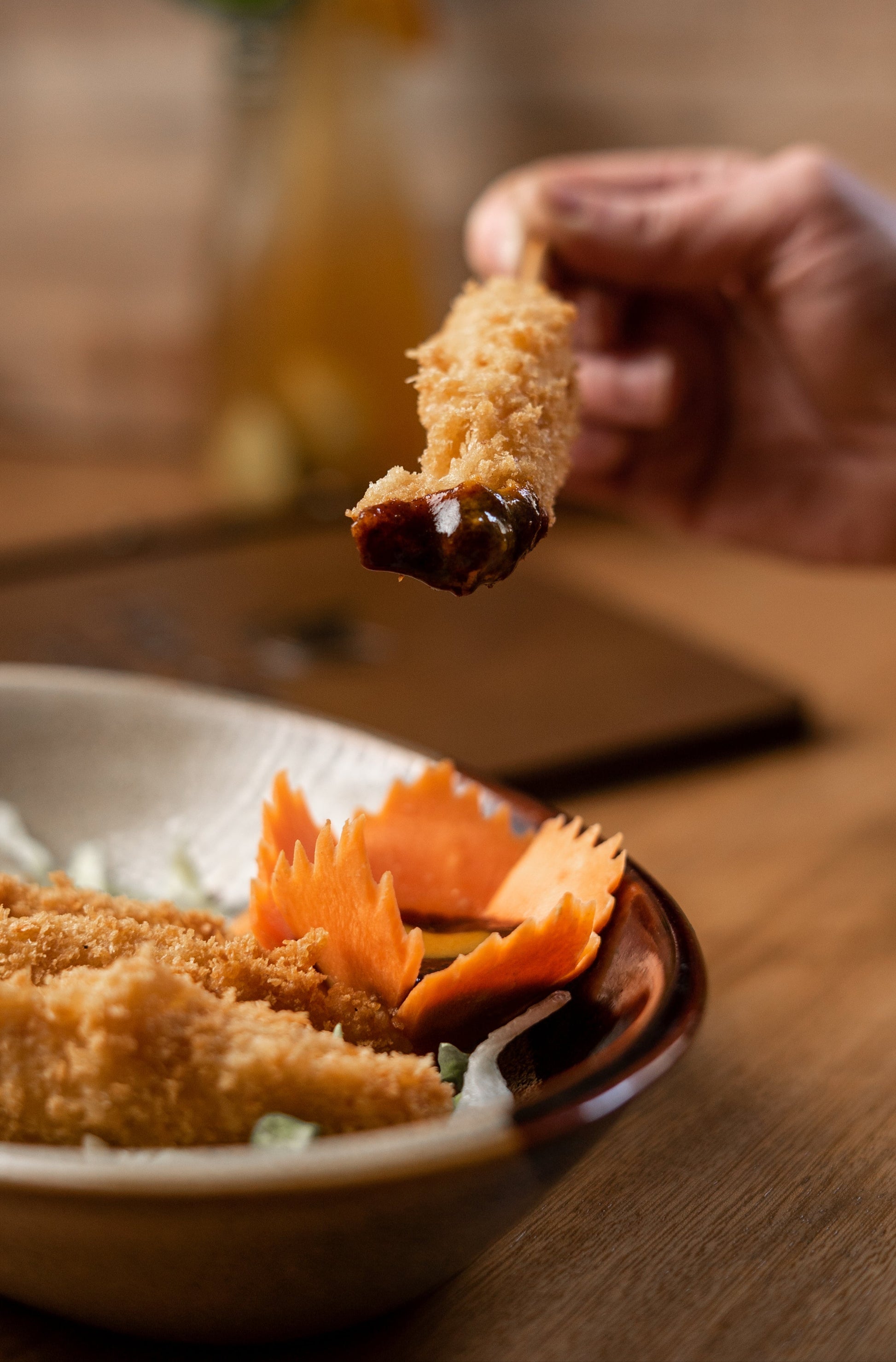 Hand holding a fried Asian bite dipped in Black Magic Plum sauce over a plate of food