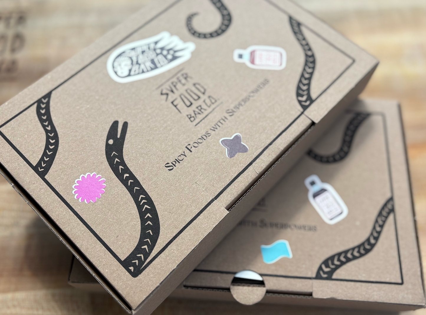 Two closed Superfood Bar Co. gift boxes stacked on top of each other, featuring bold label designs and product stickers