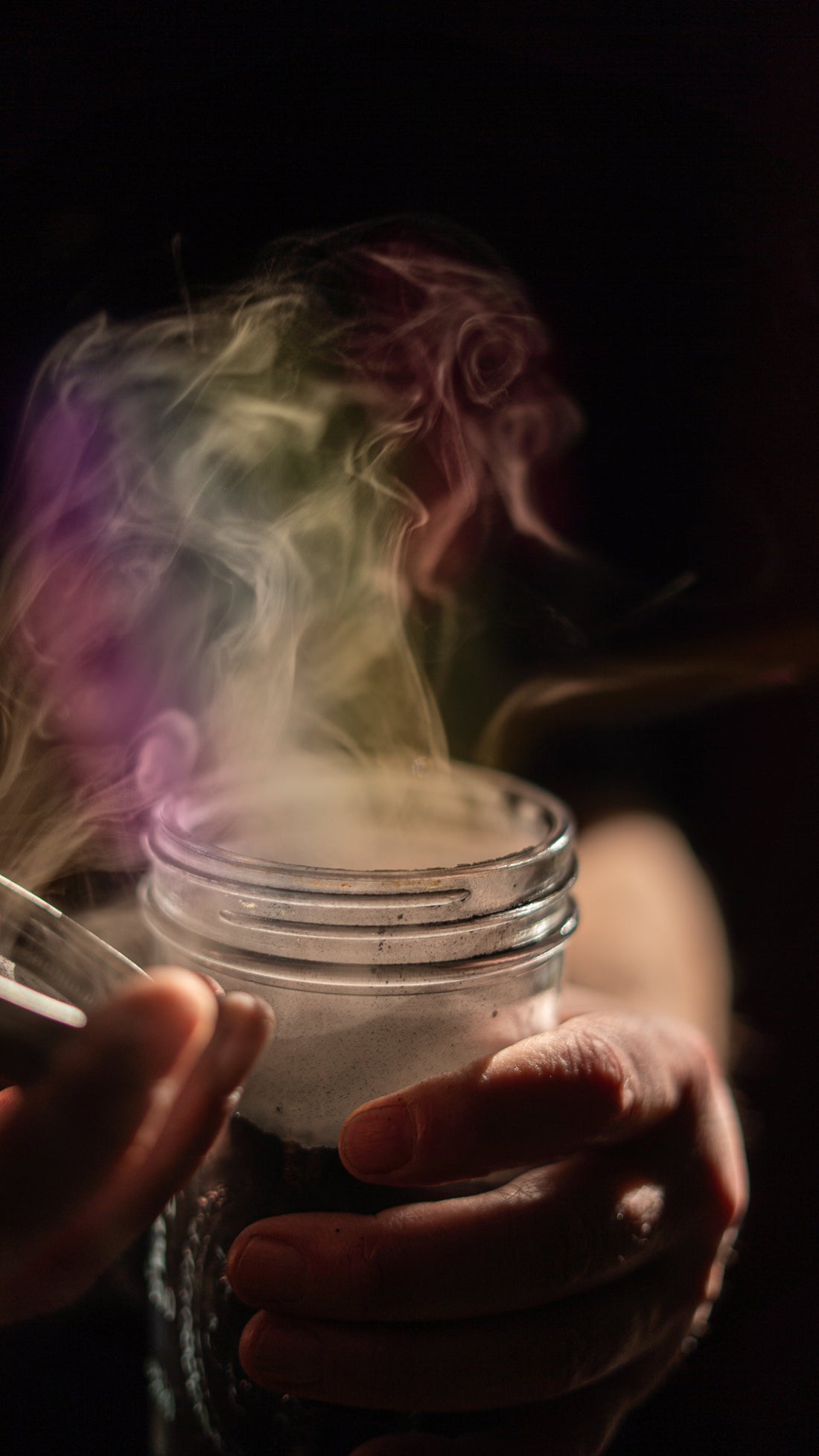 Man holding a glass jar with smoke rising from it, creating a mysterious, atmospheric scene