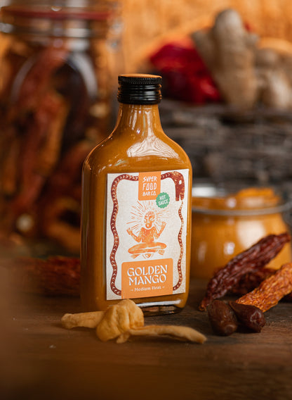 Golden Mango hot sauce bottle on a rustic table with chef’s hands in the background